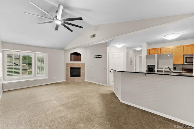 unfurnished living room featuring vaulted ceiling, sink, a fireplace, light carpet, and ceiling fan