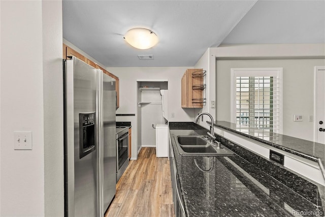 kitchen featuring dark stone counters, sink, stove, stainless steel fridge, and light hardwood / wood-style flooring