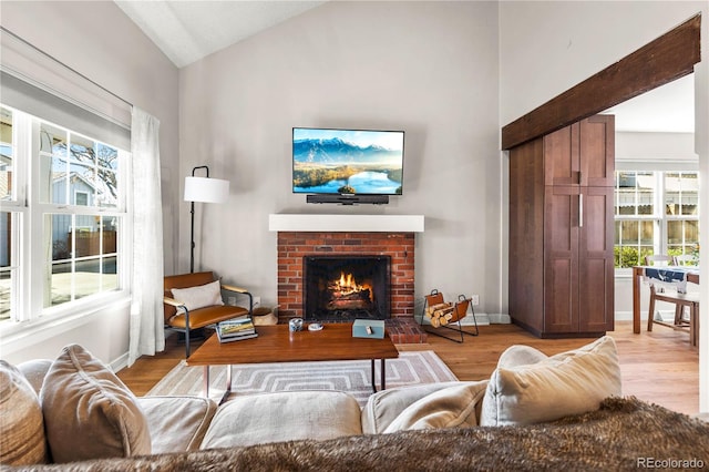 living area featuring a healthy amount of sunlight, baseboards, a brick fireplace, and wood finished floors