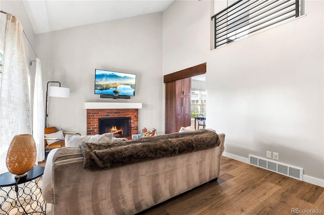 living area with visible vents, a brick fireplace, wood finished floors, high vaulted ceiling, and baseboards