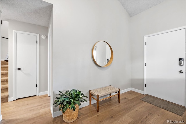 entrance foyer with baseboards, a textured ceiling, light wood-style flooring, and stairs