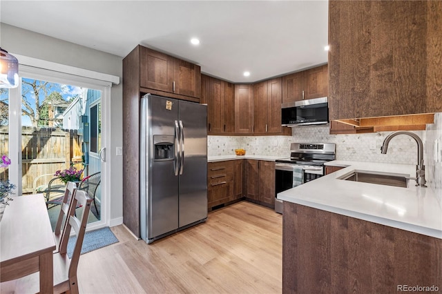 kitchen with decorative backsplash, a sink, light countertops, light wood-style floors, and stainless steel appliances