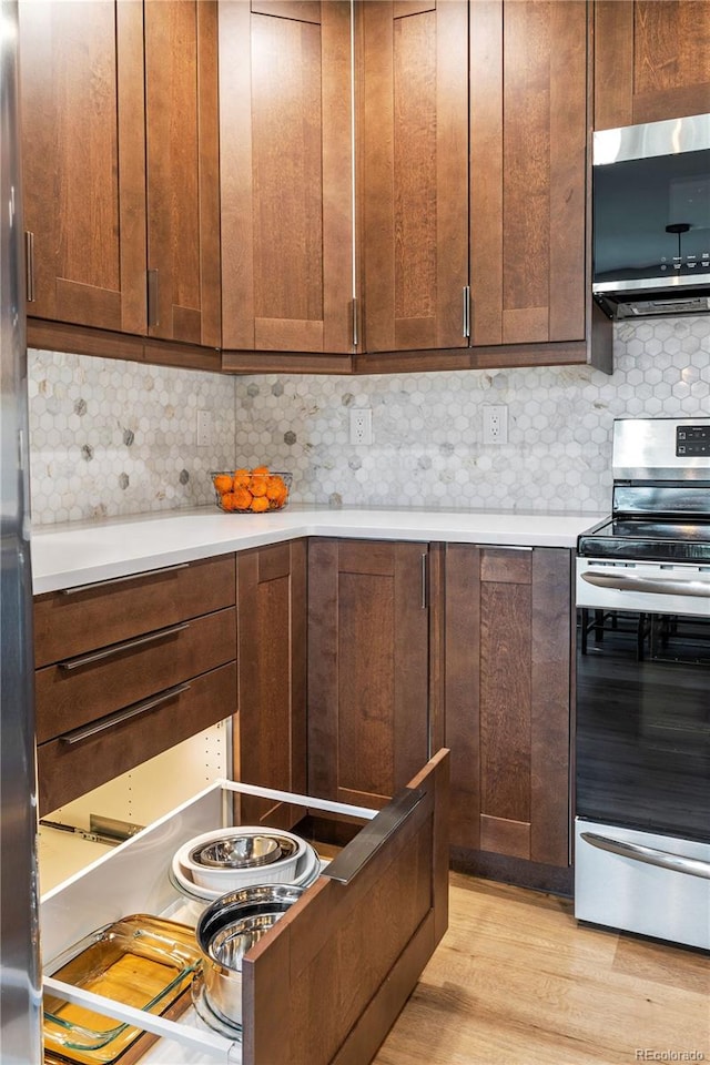 kitchen with light countertops, decorative backsplash, stainless steel appliances, and light wood finished floors