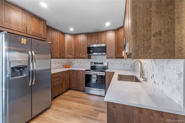 kitchen featuring appliances with stainless steel finishes, a sink, light countertops, light wood-style flooring, and decorative backsplash