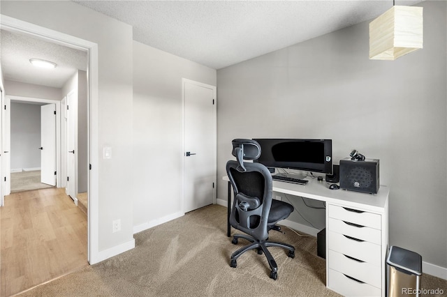 office featuring baseboards, a textured ceiling, and light colored carpet