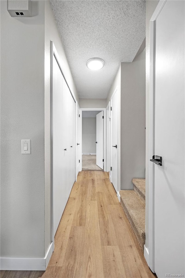 hall with a textured ceiling, baseboards, and light wood-type flooring