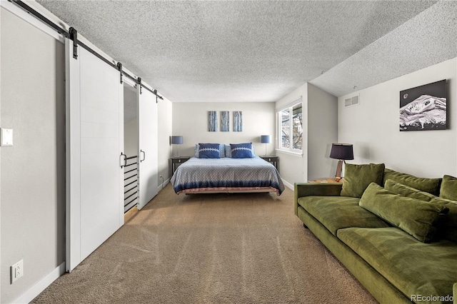 carpeted bedroom with a textured ceiling, baseboards, a barn door, and visible vents