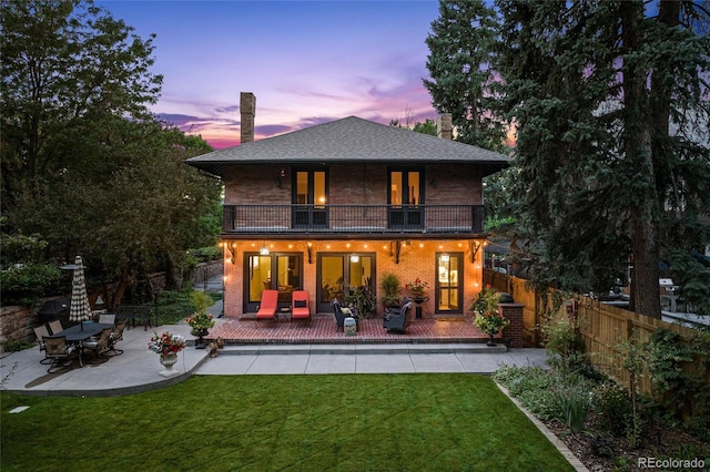 rear view of house with a patio, a balcony, brick siding, fence, and a yard