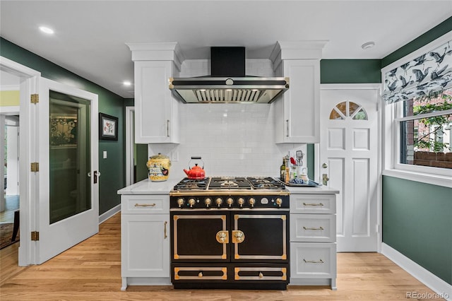 kitchen with wall chimney exhaust hood, white cabinetry, and double oven range