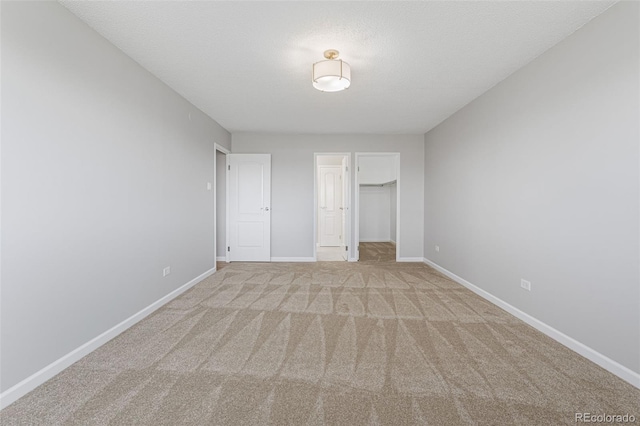 unfurnished bedroom featuring a walk in closet, light carpet, a closet, and a textured ceiling