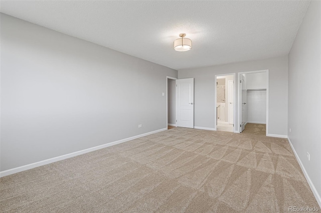 unfurnished bedroom with connected bathroom, a textured ceiling, light carpet, a spacious closet, and a closet