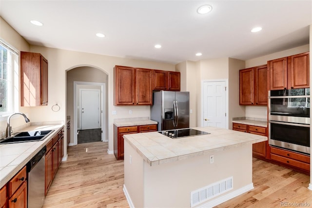 kitchen featuring appliances with stainless steel finishes, tile countertops, light wood-type flooring, sink, and a center island