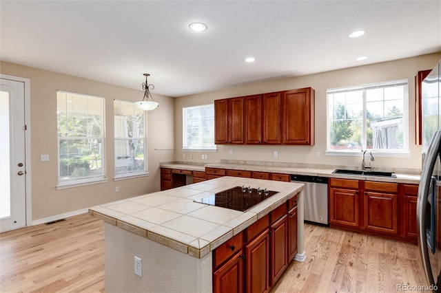 kitchen with appliances with stainless steel finishes, sink, light wood-type flooring, a kitchen island, and hanging light fixtures