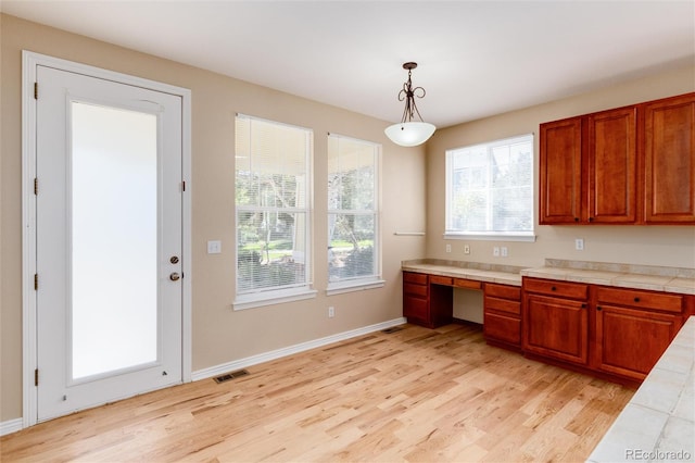 kitchen featuring tile countertops, light hardwood / wood-style flooring, built in desk, and hanging light fixtures