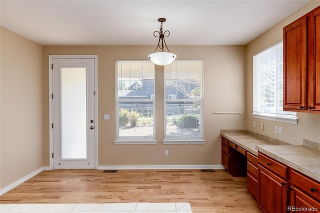 interior space with built in desk, tile countertops, light wood-type flooring, and hanging light fixtures