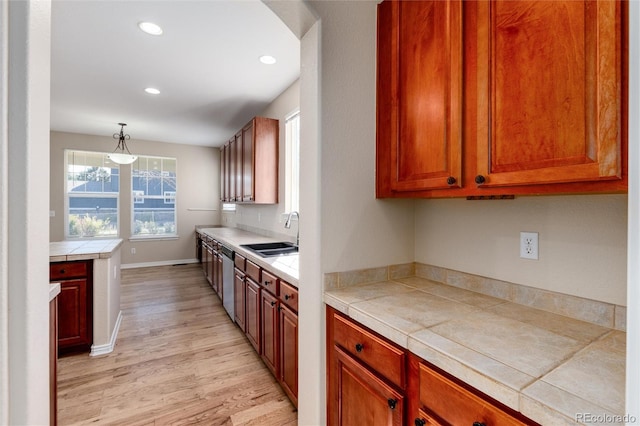 kitchen with sink, dishwasher, pendant lighting, tile counters, and light hardwood / wood-style flooring