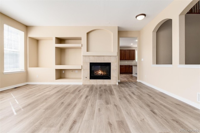 unfurnished living room featuring light hardwood / wood-style flooring, a fireplace, and built in shelves