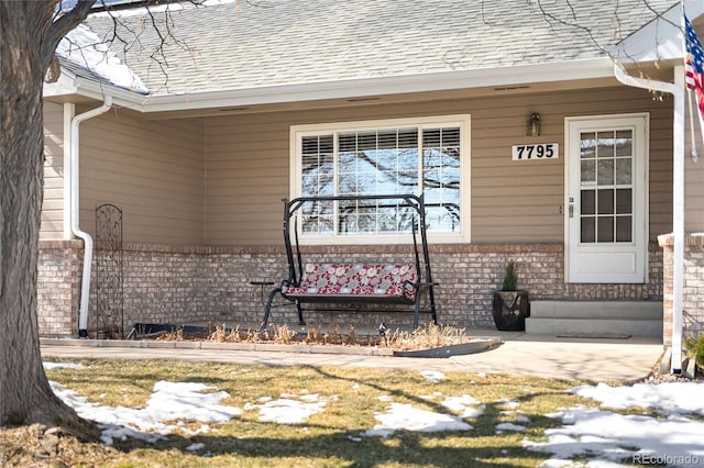 doorway to property with a shingled roof and brick siding