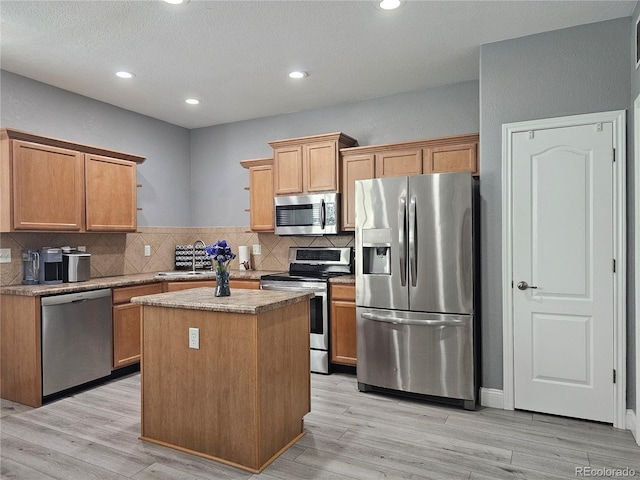 kitchen featuring decorative backsplash, light wood-type flooring, stainless steel appliances, sink, and a center island