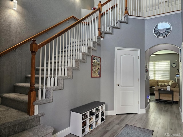 stairs with arched walkways, hardwood / wood-style floors, a towering ceiling, and baseboards