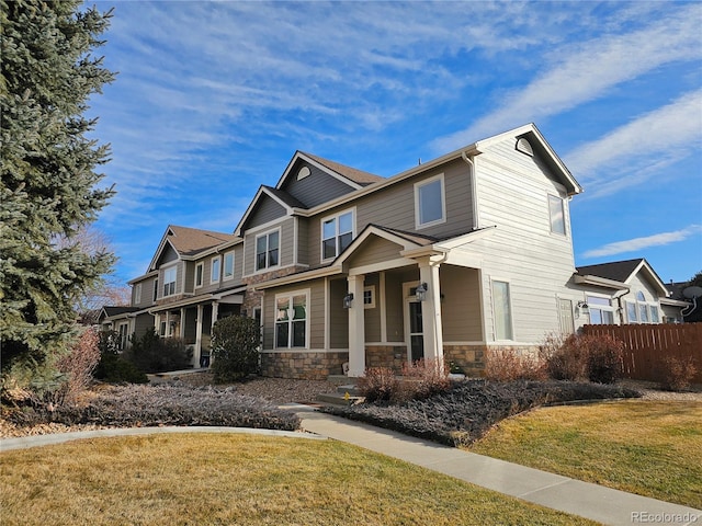 craftsman inspired home featuring stone siding, fence, and a front lawn