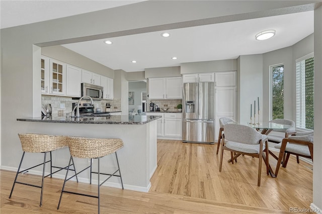 901 Sage Sparrow Cir, Highlands Ranch, CO 80129 - kitchen featuring stainless steel appliances, glass insert cabinets, light wood finished floors, dark stone countertops, and white cabinetry