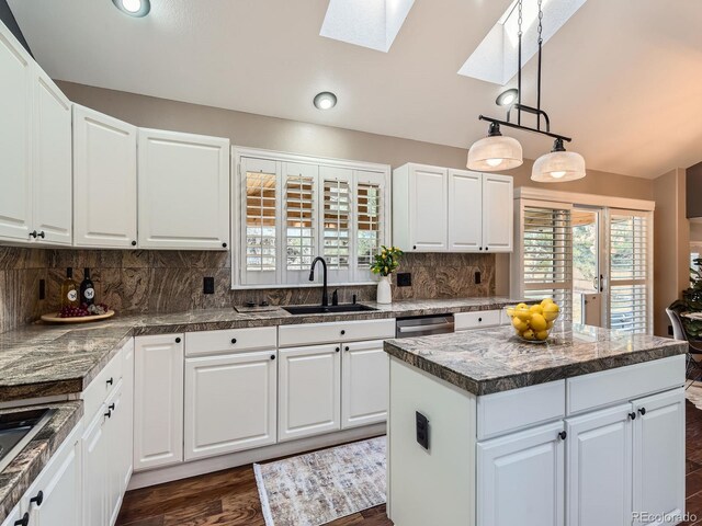 kitchen featuring white cabinets, vaulted ceiling with skylight, backsplash, and a sink