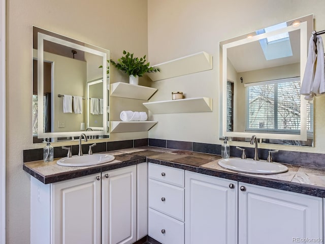 bathroom featuring double vanity, a skylight, and a sink