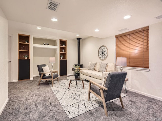 carpeted living area featuring a wood stove, baseboards, visible vents, and recessed lighting