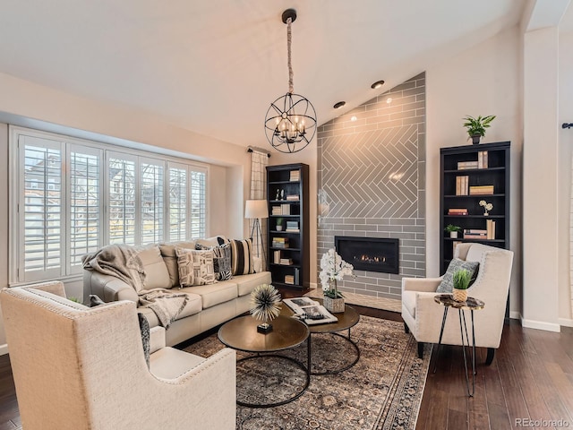 living area featuring dark wood-style flooring, a fireplace, lofted ceiling, a chandelier, and baseboards