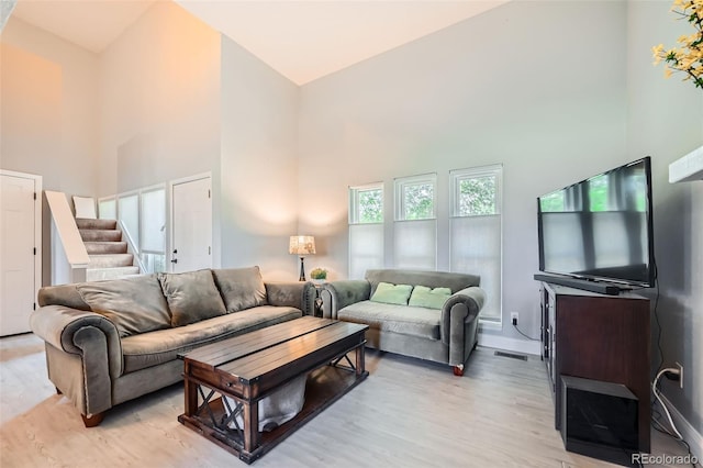 living room featuring high vaulted ceiling, light wood-type flooring, stairs, and baseboards
