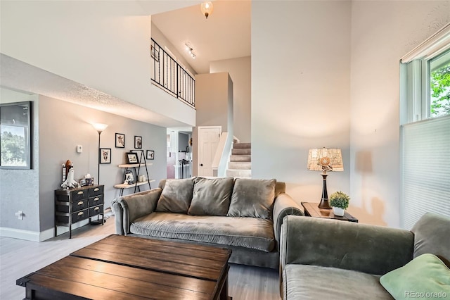 living area featuring stairs, wood finished floors, baseboards, and a high ceiling