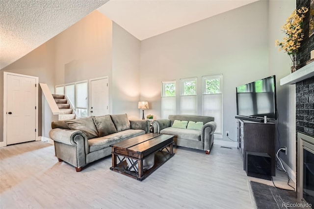 living area featuring high vaulted ceiling, light wood-type flooring, a fireplace with flush hearth, baseboards, and stairs