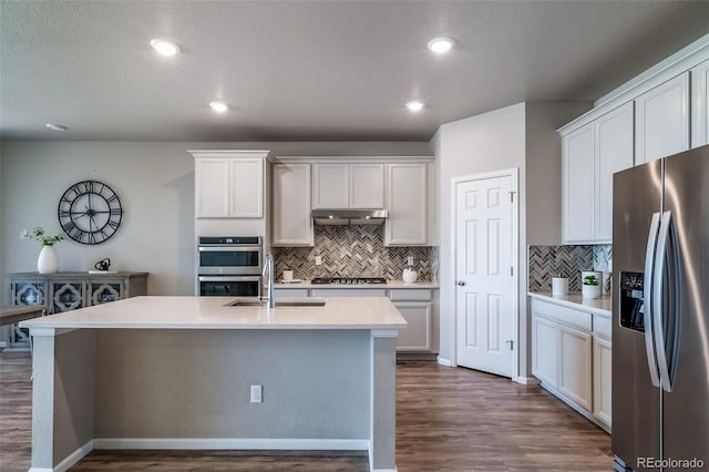 17028 Osage St, Broomfield, CO 80023 - kitchen featuring stainless steel appliances, under cabinet range hood, dark wood-style flooring, decorative backsplash, and a kitchen island with sink