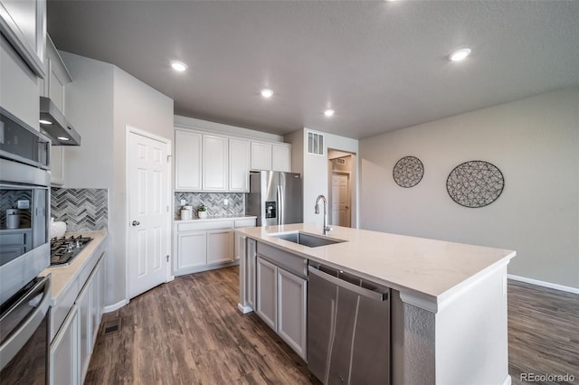 17028 Osage St, Broomfield, CO 80023 - kitchen with appliances with stainless steel finishes, tasteful backsplash, dark wood-style floors, white cabinetry, and a kitchen island with sink