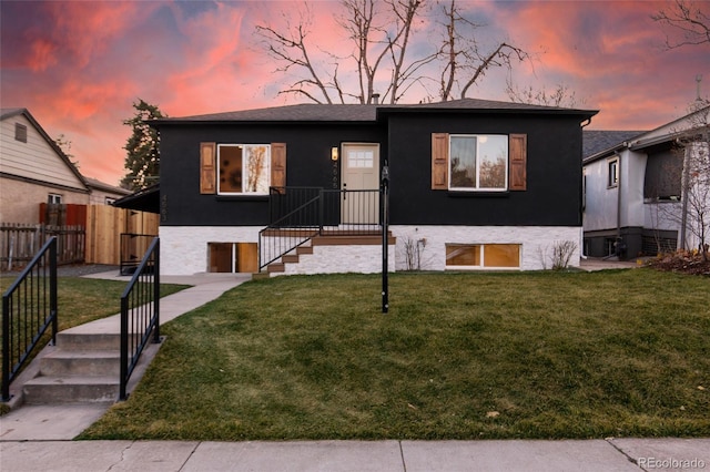 view of front of house with stucco siding, a lawn, and fence