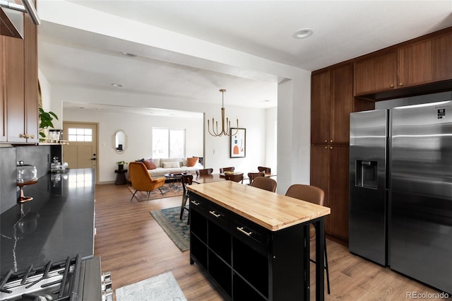 kitchen with light wood finished floors, open floor plan, a breakfast bar, a notable chandelier, and stainless steel fridge