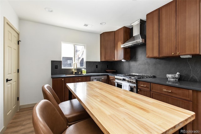 kitchen featuring tasteful backsplash, visible vents, wall chimney range hood, stainless steel appliances, and a sink