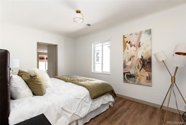 bedroom featuring visible vents, multiple windows, baseboards, and wood finished floors