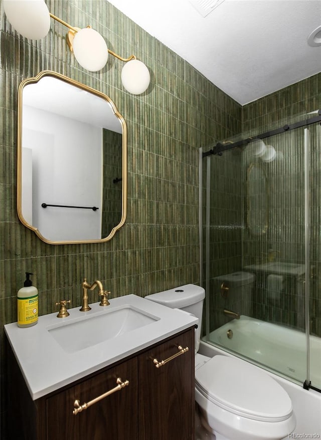 full bathroom featuring shower / bath combination with glass door, tile walls, vanity, and toilet