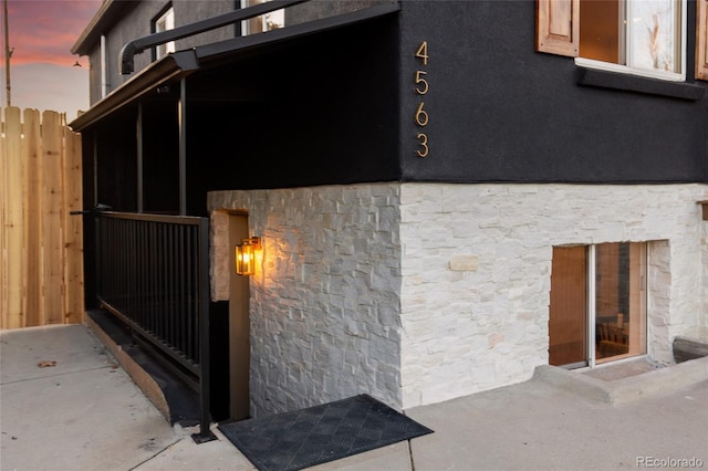 exterior space featuring stucco siding, stone siding, and fence