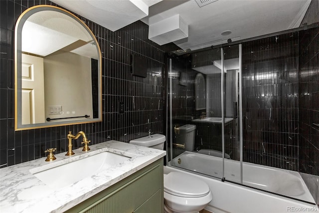 bathroom with bath / shower combo with glass door, toilet, vanity, decorative backsplash, and tile walls