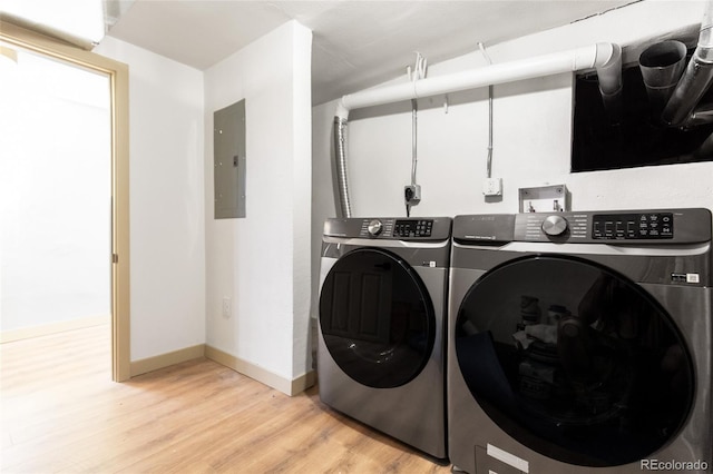 clothes washing area with baseboards, light wood finished floors, washing machine and clothes dryer, laundry area, and electric panel