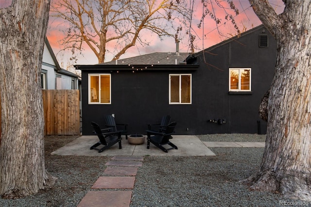 back of property at dusk featuring stucco siding, a fire pit, a patio, and fence