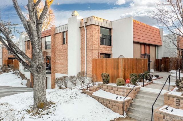 view of snowy exterior with brick siding and fence