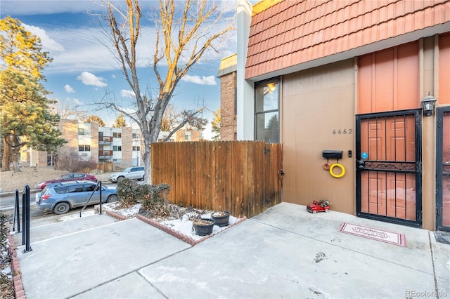 exterior space featuring a tile roof, fence, and mansard roof