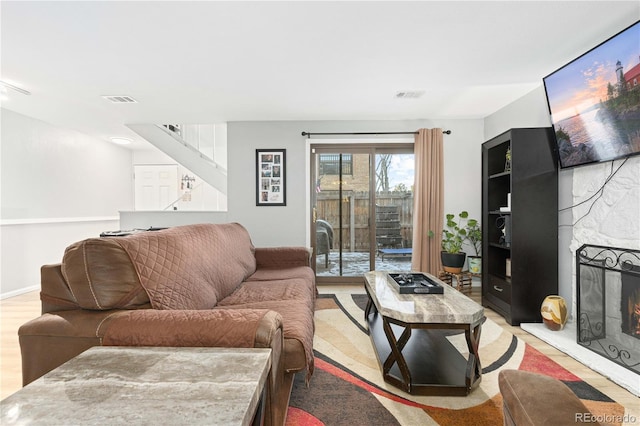 living area featuring a stone fireplace, light wood-type flooring, visible vents, and baseboards