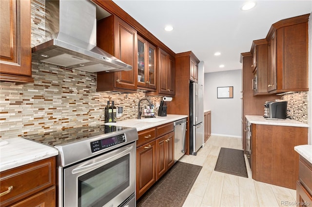 kitchen with stainless steel appliances, tasteful backsplash, glass insert cabinets, a sink, and wall chimney range hood