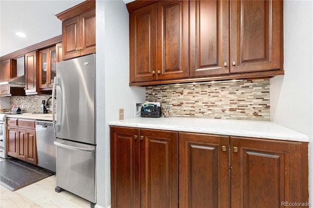 kitchen featuring decorative backsplash, wall chimney exhaust hood, light stone counters, glass insert cabinets, and stainless steel appliances