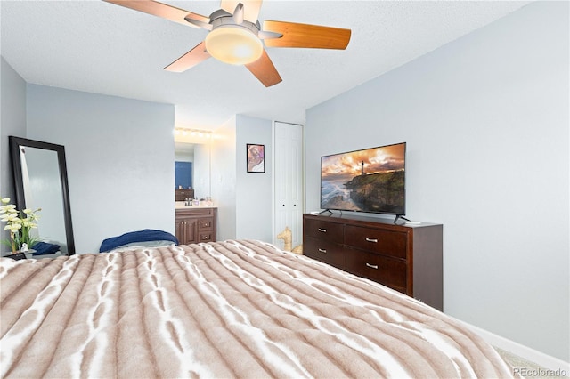 bedroom featuring baseboards, ensuite bath, ceiling fan, a textured ceiling, and a closet